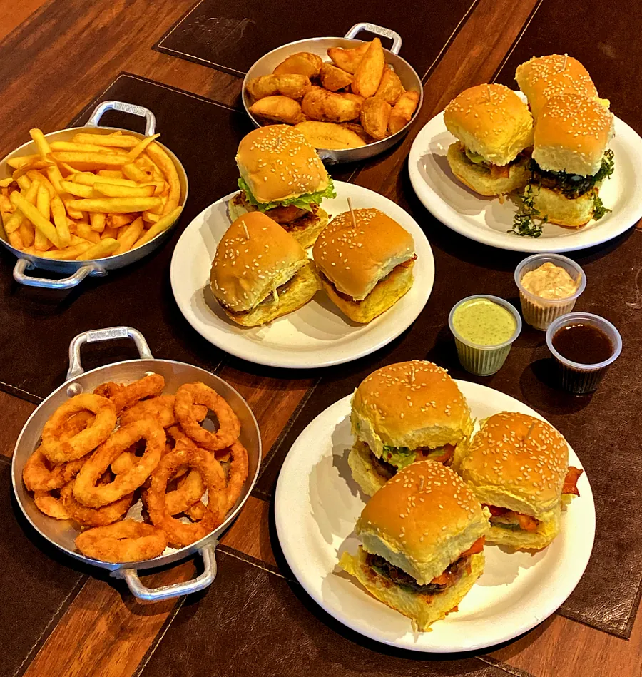 Mesa do rodízio com mini-hambúrgueres, batata palito, batata rústica, onion rings e molhos